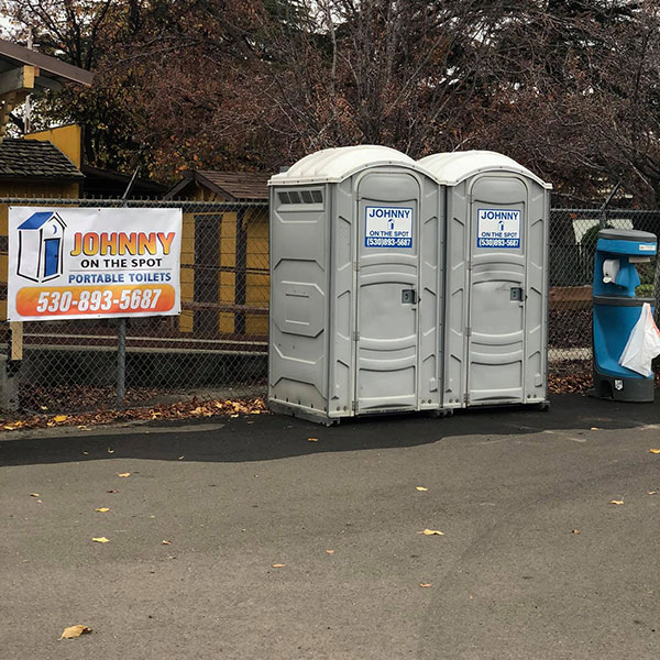 two grey porta potty units in front of yellow building