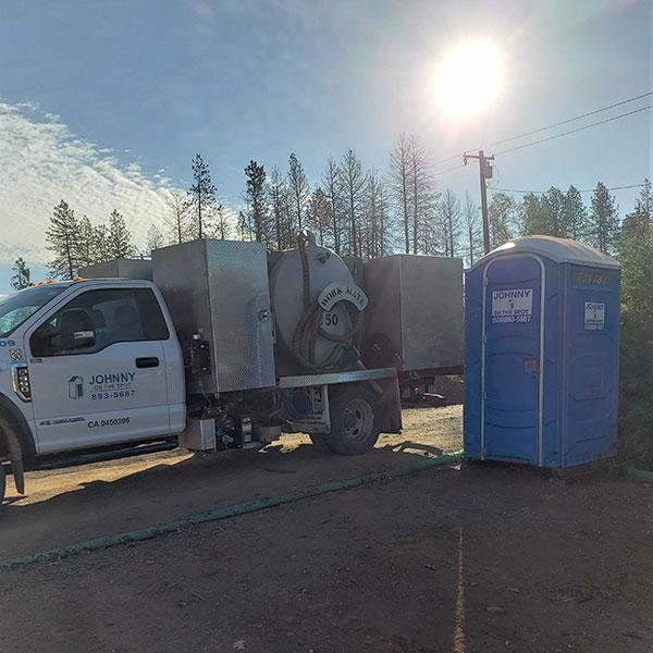 Johnny on the Spot truck servicing a blue construction porta potty